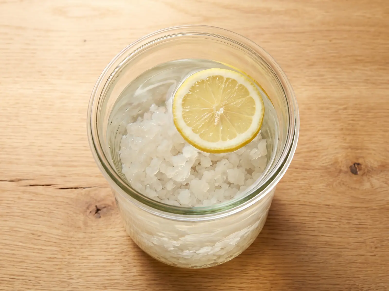 wasserkefir rezepte Glas mit Wasserkefir, Kefirkristallen und einer Zitronenscheibe von oben auf hellem Untergrund.
