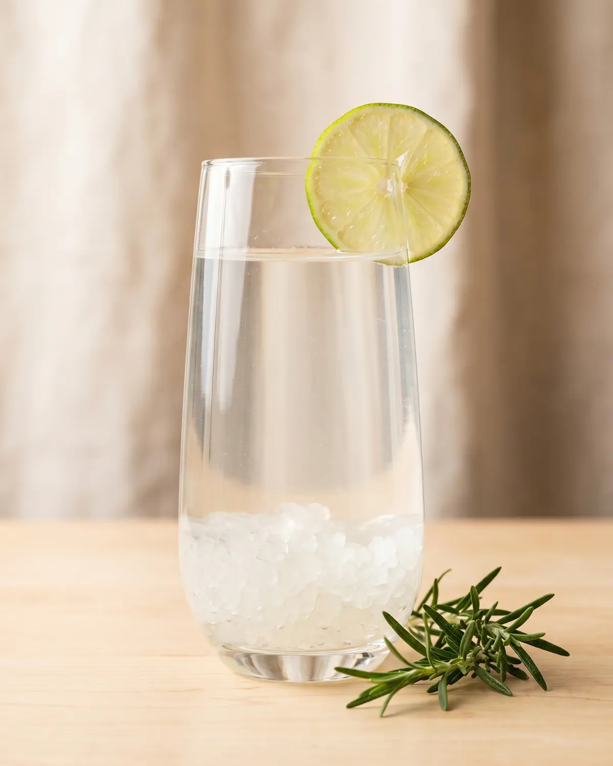wasserkefir für anfänger Ein Glas Wasserkefir mit Limettenscheibe, frischem Rosmarin und hellem Licht von oben auf der Oberfläche.