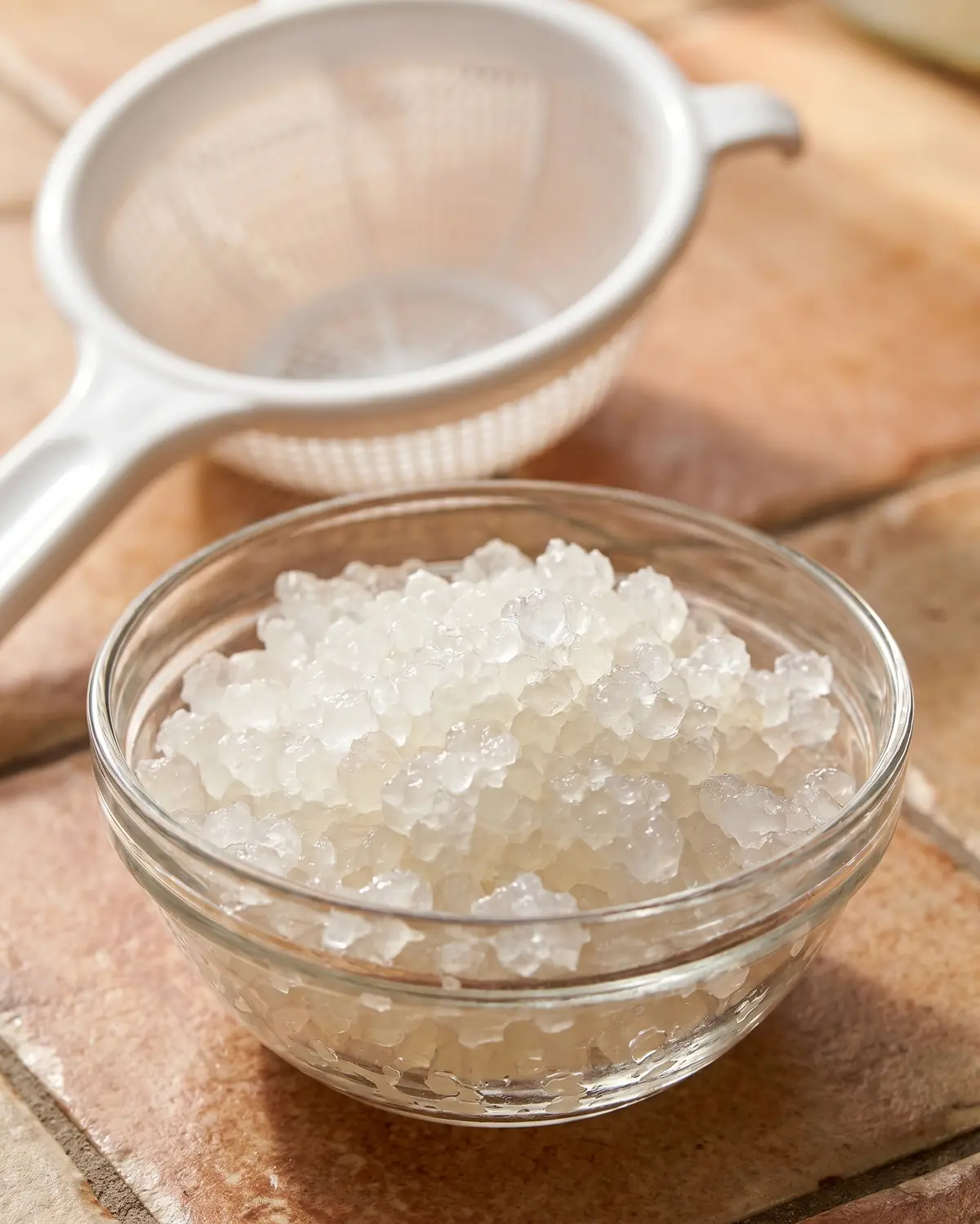 wasserkefir kristalle werden kleiner Frisch abgesiebte, glasige Wasserkefir-Körnchen liegen in einer kleinen Schale neben einem hellen Sieb.