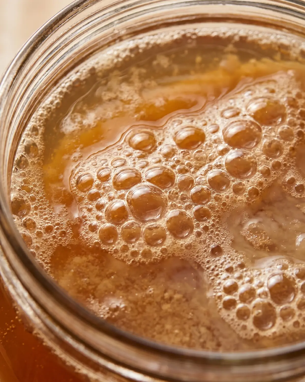 kombucha selber machen Nahaufnahme von feinen Blasen auf bernsteinfarbenem Kombucha in einem angeschnittenen Glasrand.