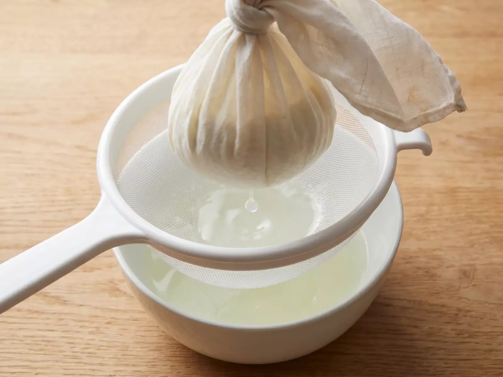 unterschied kefir joghurt Abgetropfter Joghurt in einem mit Tuch ausgelegten Sieb, während ein Tropfen Molke herabfällt.